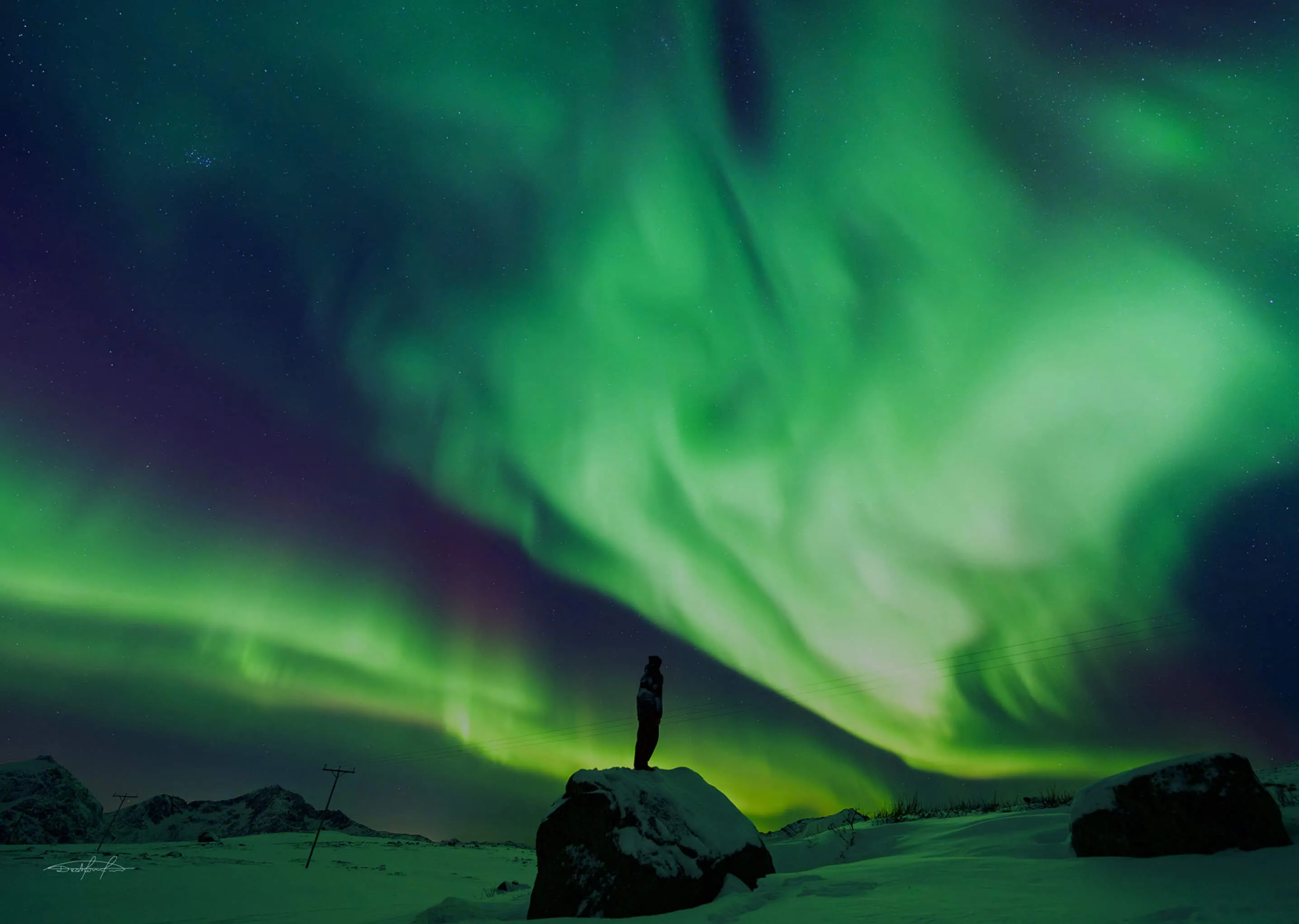 Grønt nordlys over en person på en fjellknaus